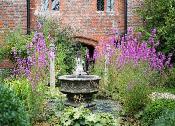 A garden with flowers in bloom and a stone water fountain.