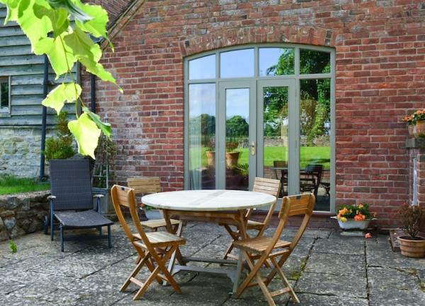 a paved patio with outdoor dining furniture, sun lounger and French windows into a house.