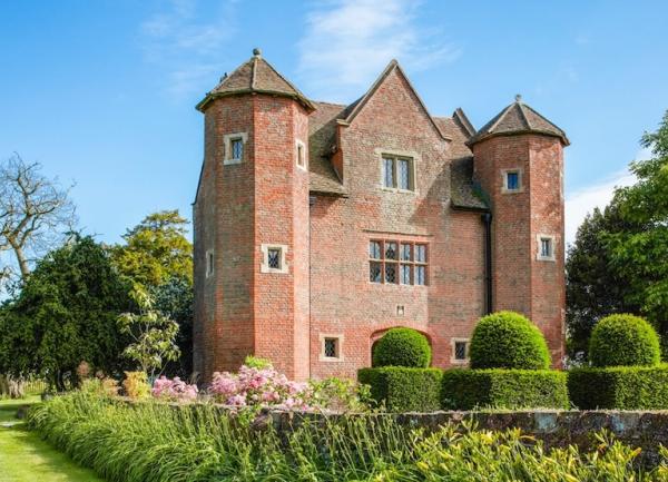 Exterior of a 3-storey, brick-built Tudor house with twin turrets and walled garden.