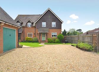 A modern New Forest holiday home overlooks a large shingle drive and a garage.