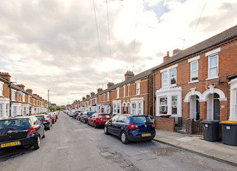 A terrace of brick-built Victorian houses with large bay windows overlook a street.