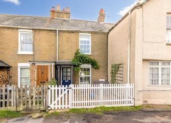 A stone-built terraced cottage with a front garden behind a picket fence.