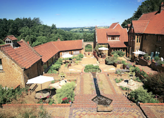 A flower-filled, paved formal garden courtyard surrounded by large and small barn conversions