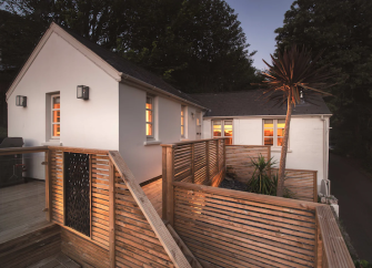 A modern Ilfracombe holiday cottage surrounded by a split level wooden deck at dusk.