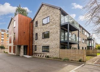 A Modern 3-storey apartment block with large glass-fronted balconies with outdoor dining furniture.