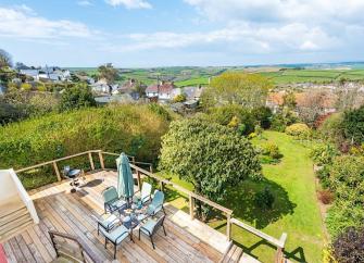 A 1st floor deck with outdoor dining furniture overlooks a garden and South Devon countryside.