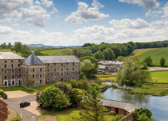 A converted 3-storey mill building overlooking lawns and a lake.