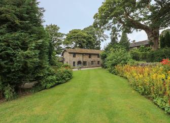 A Somerset stone barn conversion overlooks a large lawn lined by flower beds and shrubs.