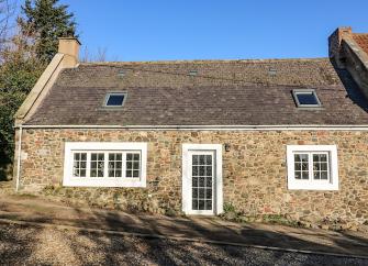 Exterior of a stone-built single storey cottage with a slate roof overlooking an empty cobbled street.