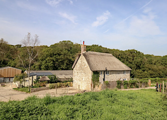 Exterior of a thatched Abbotsbury holiday cottage with farm buildings behind.