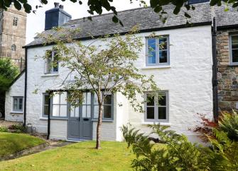 Exterior of a two-storey Devon holiday cottage with rendered walls and a slate roof overlooking a lawn.