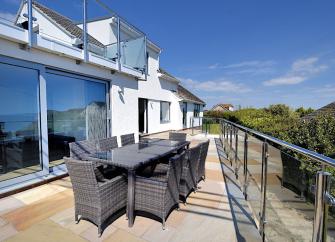 A terrace with dining facilities lies in front of a long, 2-storey, contemporary house.