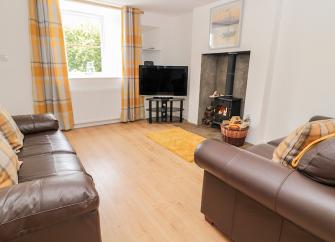 A spacious wooden floored lounge with twin sofas, TV and a woodburner.