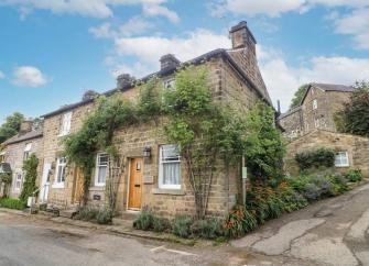 A vine-clad, stone-built, corner cottage on an empty village street.