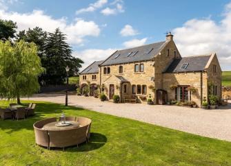 Exterior of a large stone-built Dales farmhouse with 2 wings, a large lawn and fields all around it.