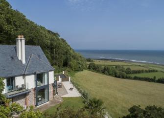 A large contemporary holiday cottage overlooks fields dipping down to a beach and ocean views.