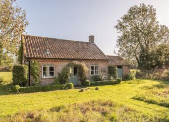 Exterior of a single-story, stone cottage overlooking a large lawn.