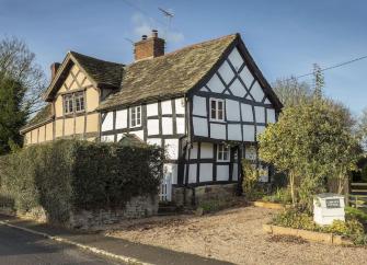A half-timbered Tudor cottage in Leominster overlooks a shingle parking space and shrub-filled garden.