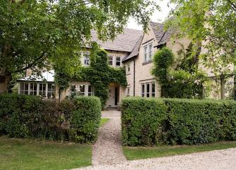 Behind a hedge is a large L-shaped contemporary cottage with a conservatory.