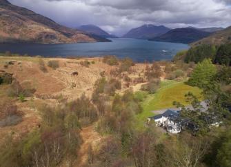 Aerial photo of a Loch in the Scottish Highlands with a holiday cottage in the foreground.