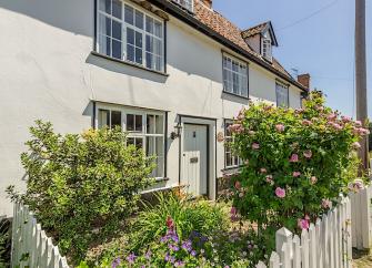 A double-fronted Sussex cottage with a flower-filled front garden behind a low picket fence.