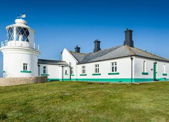 A lighthouse complex with a squat tower perches on a clifftop.