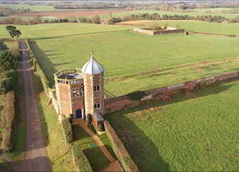 Aerial view of a tall, brick-built, twin-towered, Victorian folly in a rural location.