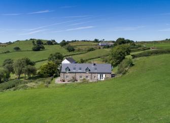 A 2-storey stone-built holiday cottage nestles in a fold a rural landscape.