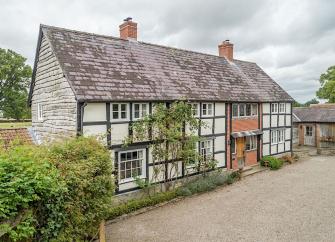 Exterior of a cross-timbered cottage overlooking a large shingle parking area.