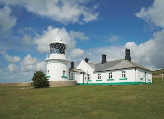 A Lighthouse tower and buildings on a grassy clifftop.