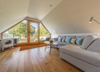 A clapper-boarded barn conversion with steps to a balcony half-hidden between trees.