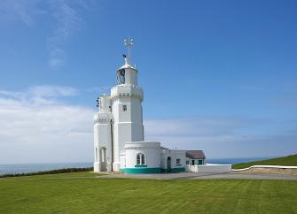 A lighthouse and cottages stand on a clifftop against an ocean background.