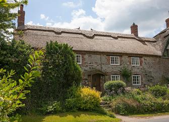 Exterior of a thatched holiday cottage in Dorset with a flower-filled garden.