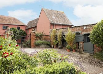 Exterior of a small Gloucestershire cottage and adjoining stable in a garden.