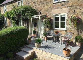 Stone-built exterior of a Peak District Cottage with flower-covered flagstone terrace.