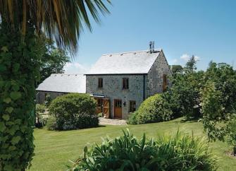 Stone-built Cornish barn conversion surrounded by shrub-lined, lawns.