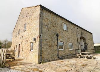 A tall, sdtone-built barn conversion with a spacious courtyard.