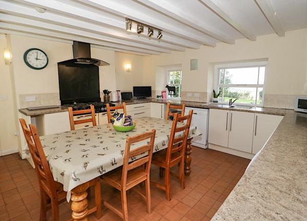 Farmhouse kitchen with terracotta tilesd, fitted floor-level cupboards, dishwasher and breakfast table seting 6.