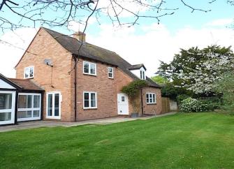 A brick-built holiday home with single storey extensions and a large, tree-lined and well-mown lawn