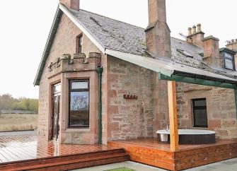 Exterior of a stone-built Highland holiday cottage with a hot-tub on its deck.