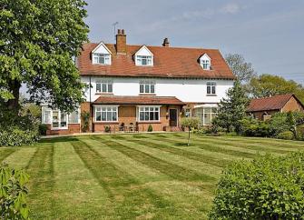 A large 1930s country house with a large well-kept lawn.