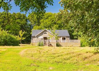 A timber eco-lodge backed by trees overlooks an open field.