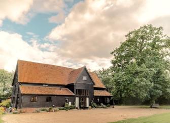 Exterior of a large Manor Farm Barn made of wood surrounded by a tree-filled garden.