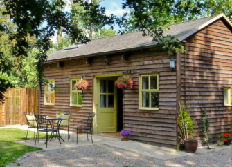 Exterior and patio of a single-storey, wooden eco-lodge surrounded by trees.