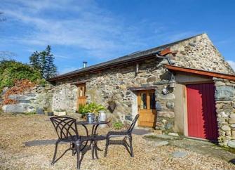 Exterior of a stone built barn conversion overlooking a  courtyard with dining table and chairs.