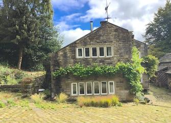 Wisteria-clad, gable end of a restored weavers cottage with two rows of windows in The Pennines.