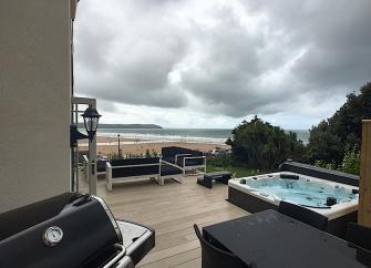 A deck with a hot tub and sun beds overlooks a surfing beach.