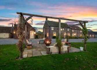 Exterior of a farm cottage and patio with a firepit at sunset.