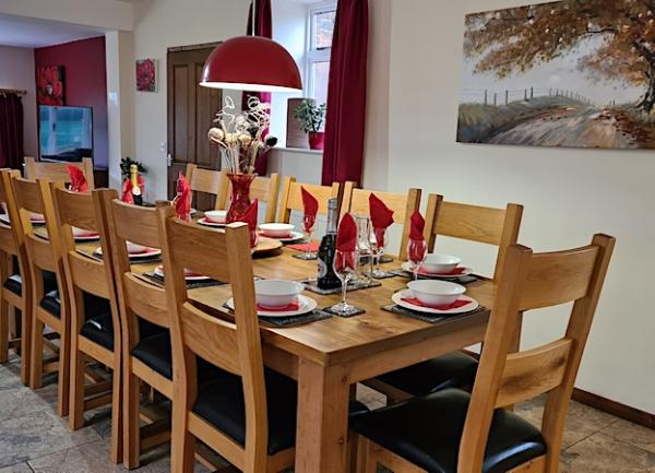 A dining area featuring a long wooden table laid for a dinner party with 10 wooden chairs and place settings.