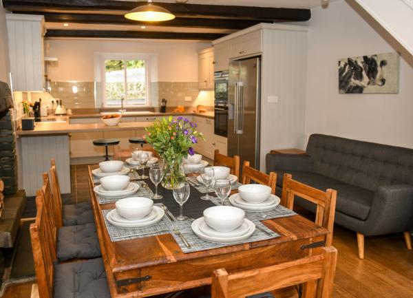 Wooden dining table laid for 8 with a kitchen beyond.
